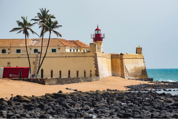São Sebastião Fort seen from the beach, with its red lighthouse and palm trees