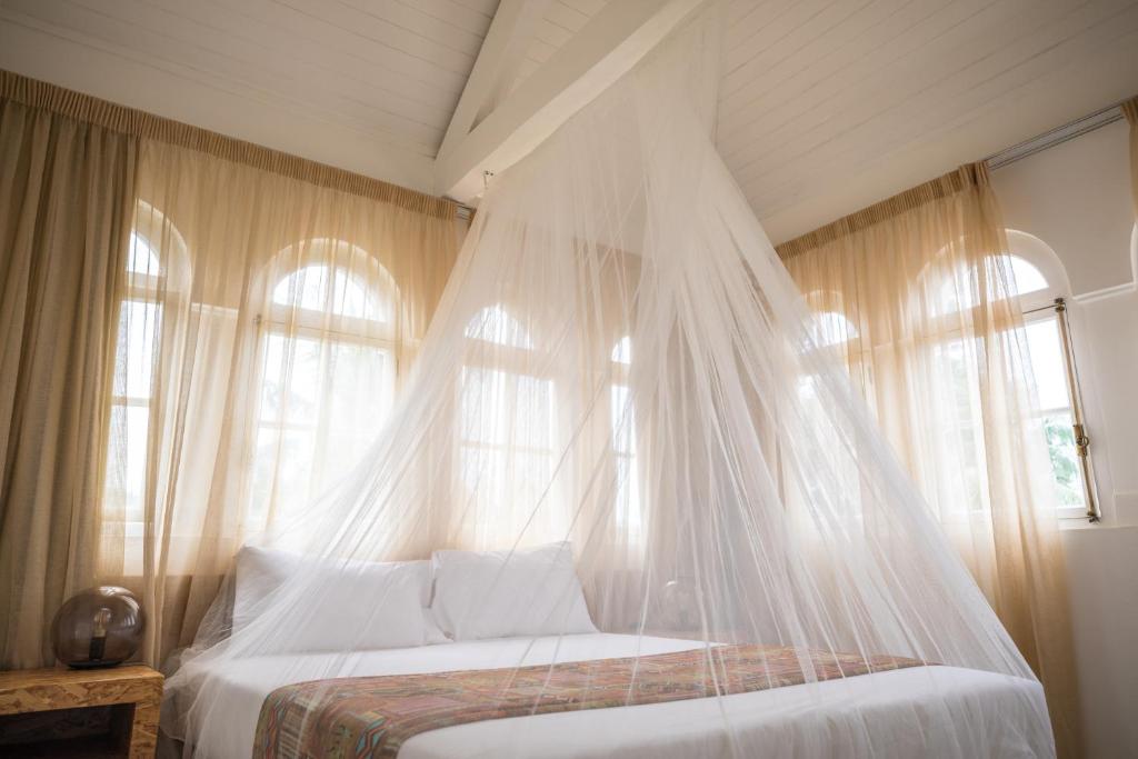 Bright guest room with a canopy bed and arched windows at Roça Santo António Ecolodge, São Tomé